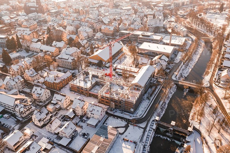 Snowy town with red construction crane standing on a construction site near a river, Zellerschule building, Nagold, Black Forest, Germany