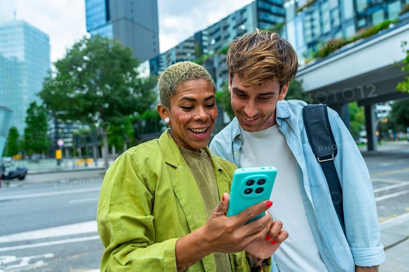 Business colleagues standing outdoors in a city, happily sharing and viewing content together on a smartphone, representing connection, communication, and collaboration