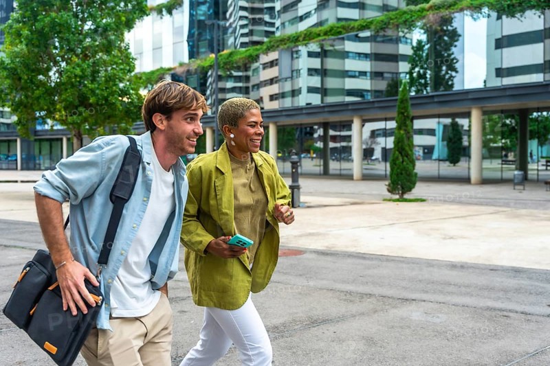 Diverse business professionals walking and discussing in a modern urban area, holding a bag and phone, reflecting concepts of teamwork, commuting, and dynamic city life