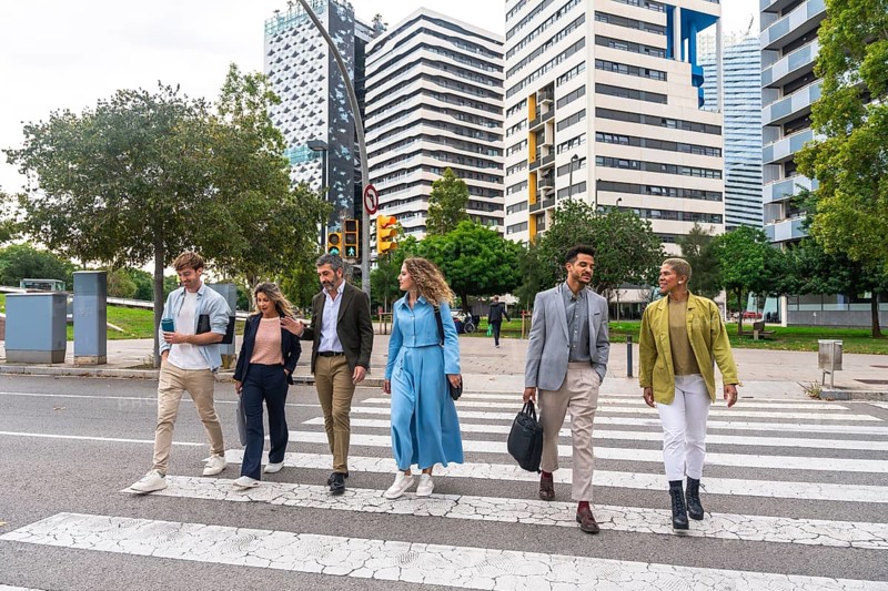 Diverse group of smiling business professionals walking together on a zebra crossing in a modern city, representing teamwork, collaboration, and urban lifestyle