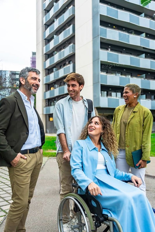 Diverse business colleagues and friends laughing and interacting outdoors in a communal city space, symbolizing teamwork, inclusion, accessibility, and modern workplace diversity