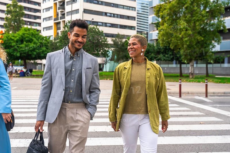 Two diverse business colleagues crossing a city street while engaging in a friendly conversation, representing collaboration, modern work life, and urban mobility