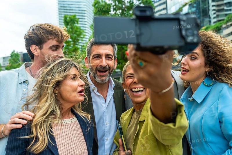 Group of diverse business professionals and colleagues enjoying a moment together, laughing and smiling while taking a collaborative selfie outdoors in an urban environment