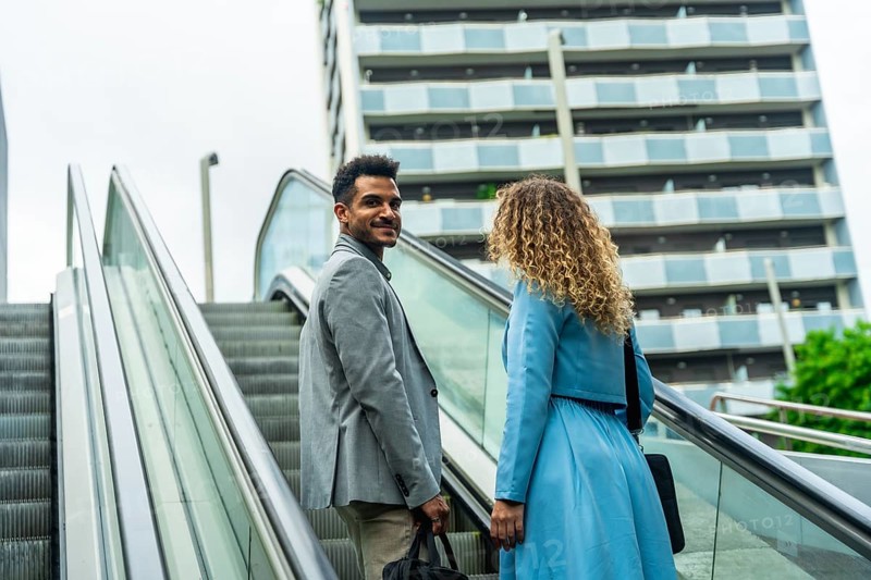 Business partners engaging in a collaborative discussion while commuting on an escalator in a modern city setting, representing urban lifestyle and career growth