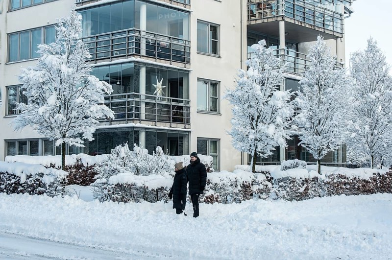 A couple walks on a snow-covered street in front of apartment buildings and snow-laden trees in Ystad, Skåne County, Sweden, Scandinavia