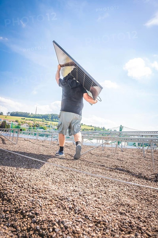 Person carrying a solar panel on a sunlit building site, new park and ride parking garage Calw Heumaden on the new Hermann Hessebahn, Calw, Germany