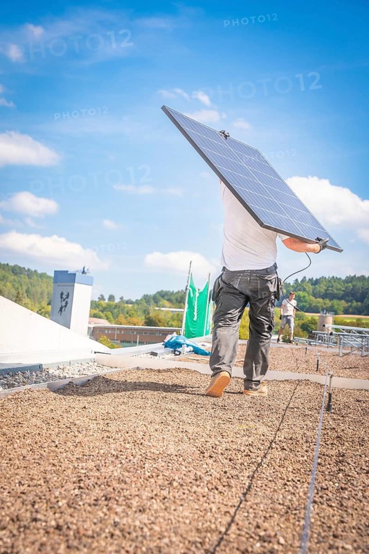 A worker carries a solar panel over the roof in sunny weather and blue skies, new park and ride parking garage Calw Heumaden on the new Hermann Hessebahn, Calw, Germany