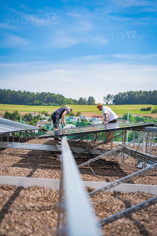 Two workers install a solar system surrounded by a quiet landscape under blue skies, new park and ride parking garage Calw Heumaden on the new Hermann Hessebahn, Calw, Germany