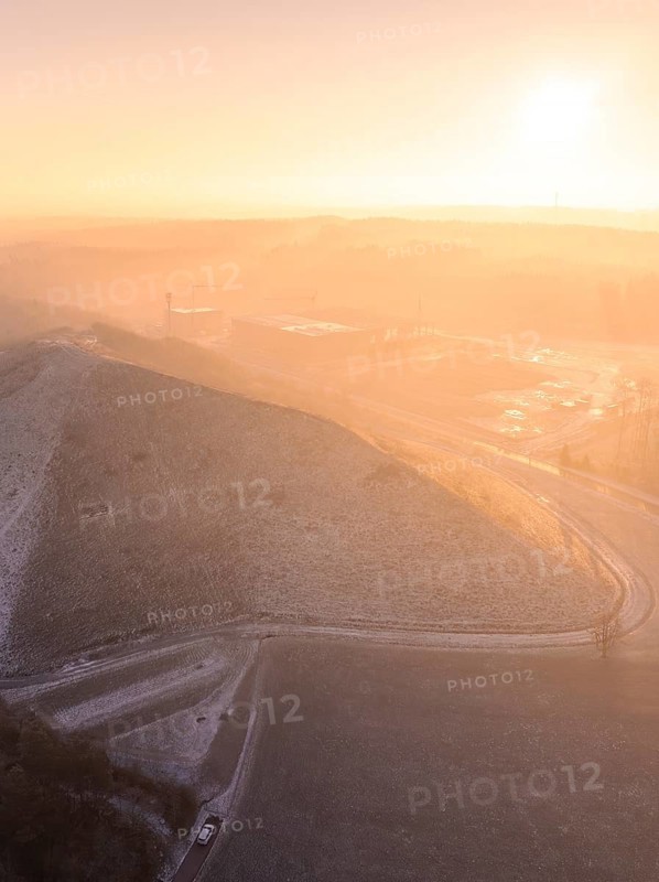 Snow-covered hilltop in soft orange light of morning sun, old deposit, construction site for PV open space plant, Lindenrain, Calw, Germany