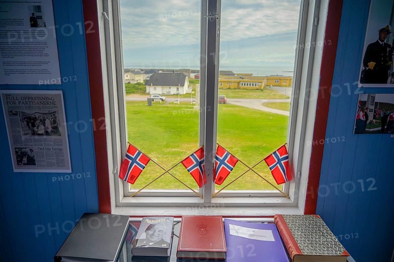 Window with Norwegian flags in the room, view of outdoor scene and books in the partisan museum in the old school of Kiberg on a wooden wall, Kiberg, Troms, Norway