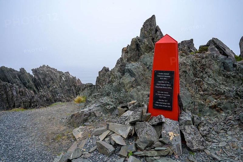 Red memorial to resistance fighters from the Second World War on rough rocks with fog in Norway, accompanied by a memorial plaque, Varanger Fjord, Barents Sea coast, Finnmark, Norway