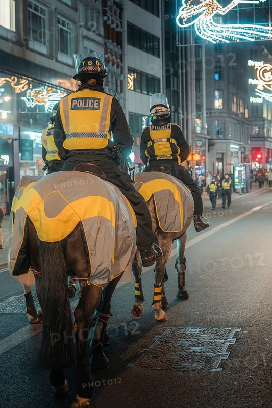 Police officers on horses patrol a brightly lit city street at night, London, England, Great Britain