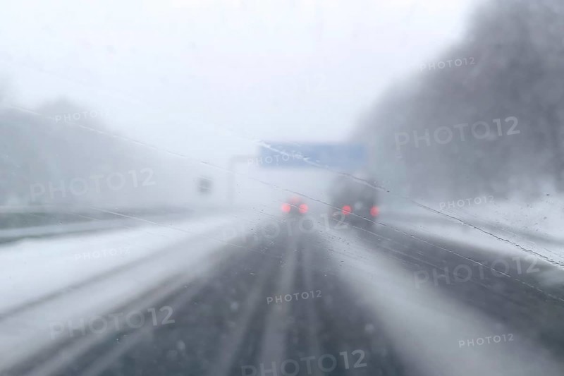 View through fogged windshield of cars driving through light snowblowing on partially covered freeway with lanes covered by snow, GermanyView through fogged windshield while driving through light snowblowing, Germany