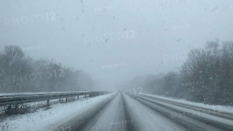 View through the windshield of a passenger car driving through light snow on an empty, partially tailored motorway without traffic with lanes covered by snow, Germany
