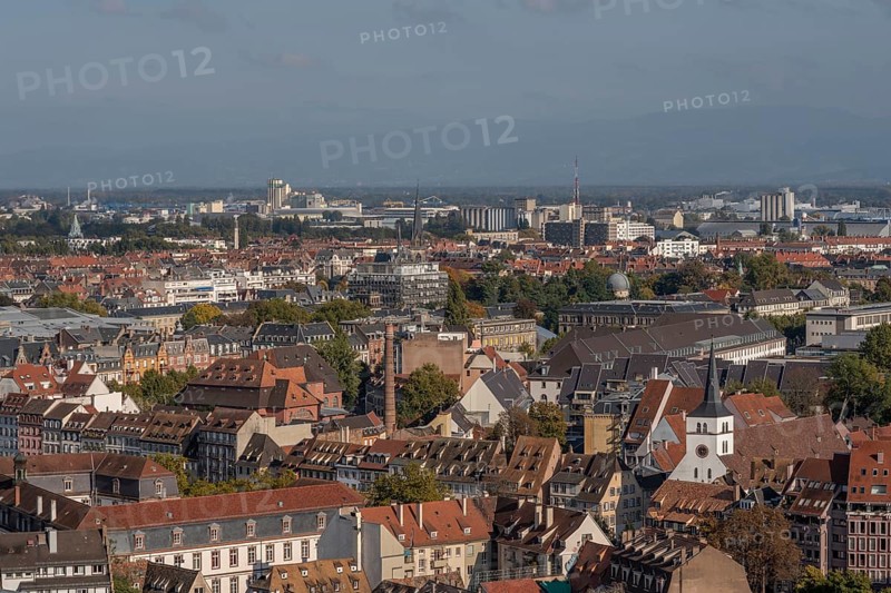 The stone balcony offers a view of the city of Strasbourg. Houses and buildings can be seen under a cloudy sky. Architectural details surround the balcony. Bas Rhin, Alsace, France
