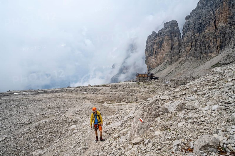 Mountaineers on a hiking trail in a rocky, cloud-covered mountain landscape while descending to Rifugio Alimonta, Brenta Mountains, Trentino, Italy