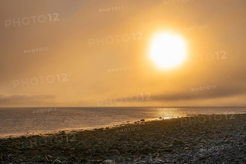 Dramatic sunset over a rocky stretch of coast with soft light, golden sky reflected in the sea, Båtsfjord, Finnmark, Norway