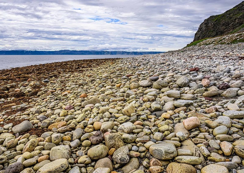 Beach with pebbles and rocks along the coast under slightly cloudy skyStore Molvik, Berlevåg, Finnmark, Norway