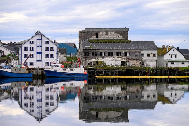 Fishing boats Fishing vessels are moored in Berlevag harbour in the north of the Varanger Peninsula with white and dilapidated buildings in the background, Berlevåg, Finnmark, Norway