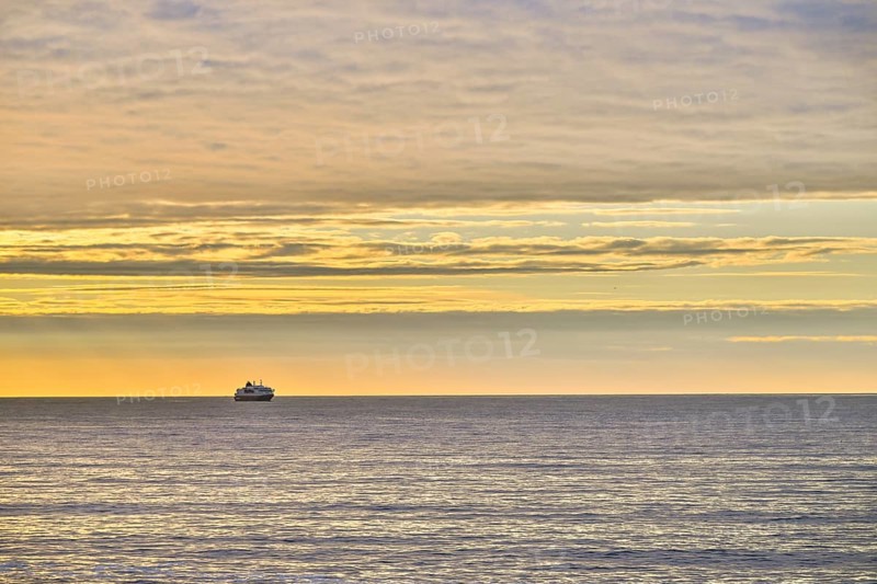 A Hurtigrute ship on the wide Barents Sea at sunset midnight sun, yellowish clouds and calm seas, Berlevåg, Finnmark, Norway