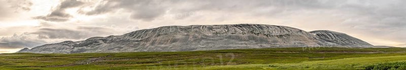 A massive granite rock mountain with bare fells dominates the landscape of the central Varanger Peninsula at Austertanaveien 890 in the foreground, green low fells vegetation wide, quiet landscape, Tana, Finnmark, Norway