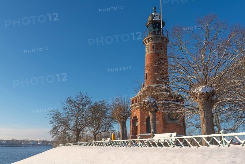 Holtenau lighthouse at the entrance of the Kiel Canal in winter, west bank of the Kiel Fjord, shipping, brick building from 1895, round tower, orientation, sea sign, beacon, ground floor with wedding room, trees, snow, blue sky, Baltic Sea, Kiel, Germany