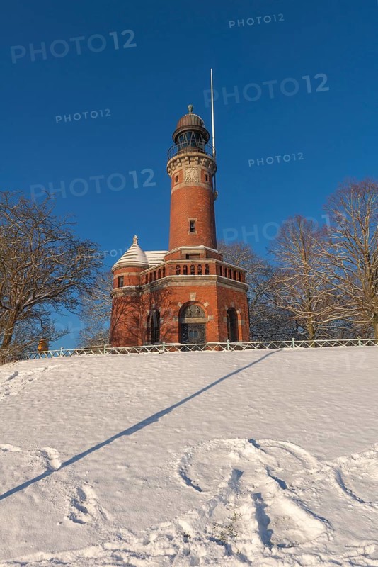 Holtenau lighthouse at the entrance of the Kiel Canal in winter, west bank of the Kiel Fjord, shipping, brick building from 1895, round tower, orientation, sea sign, beacon, ground floor with wedding room, trees, hills, snow, blue sky, Baltic Sea, Kiel, Germany