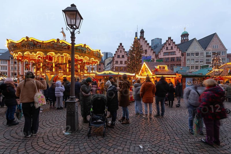 December 22, 2025, Frankfurt Christmas Market on Roemerberg with the skyline in the background at twilight. Lights are shining and a children's carousel is spinning, Frankfurt, Hesse, Germany
