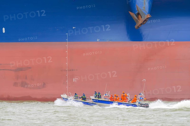 THW lifeboat with crew in orange clothing sails in front of a large ship hull on rough water, Wilhelmshafen, Jadebusen, Lower Saxony, Germany