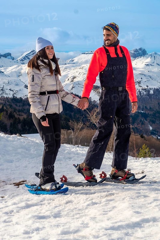 Happy couple snowshoeing in sunny snowy mountains, holding hands and smiling as they hike together through clear winter air, enjoying nature, fitness, and companionship