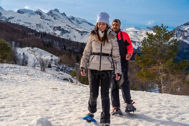Couple snowshoeing side by side through fresh deep snow in the pyrenees on a sunny winter day, enjoying outdoor adventure, fitness and togetherness in a scenic mountain landscape