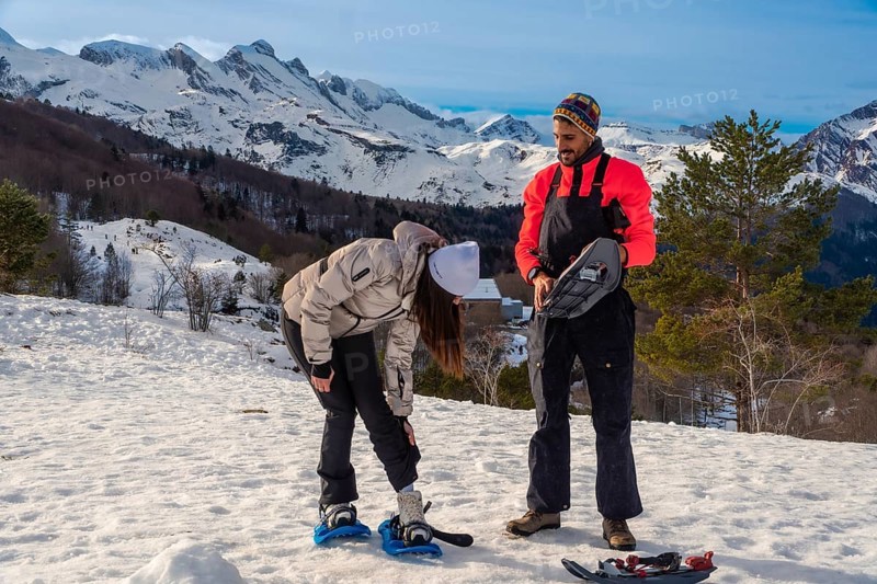 Young couple actively preparing snowshoes on a sunny winter day, ready for a trekking adventure in the snowy mountains, enjoying the clear sky and active lifestyle