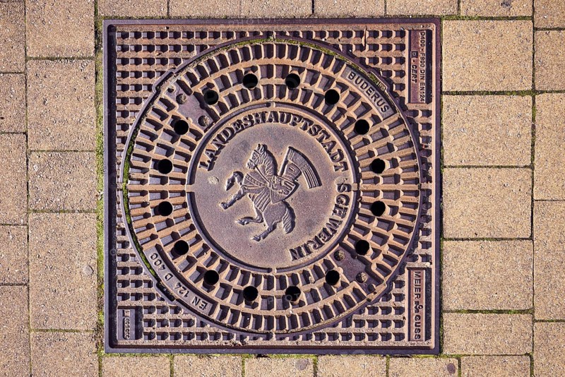 Manhole cover, city coat of arms, concrete paving stone walkway, Schwerin, state capital, district-free city, Mecklenburg-Western Pomerania, Germany