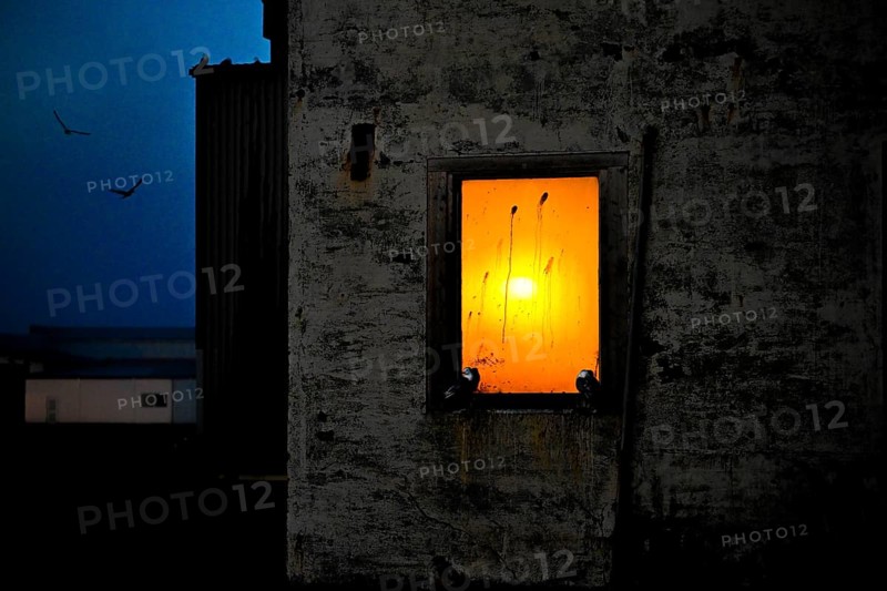 A window in a dark building through which an orange sunset shines, Vardø, Finnmark, Norway