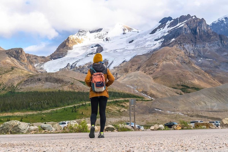 Female tourist walking towards athabasca glacier in jasper national park, alberta, canada, admiring the immensity of the glacier and surrounding mountains