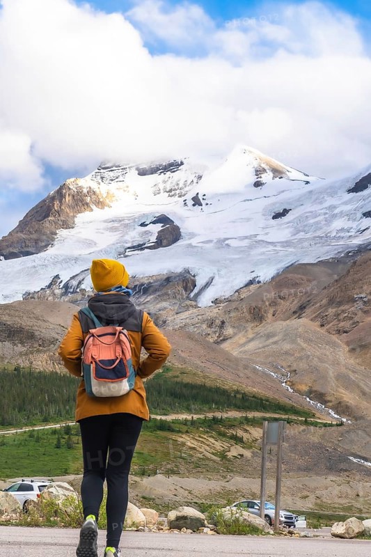 Female hiker walking towards the athabasca glacier in the columbia icefield, jasper national park on a sunny day with blue sky and some clouds