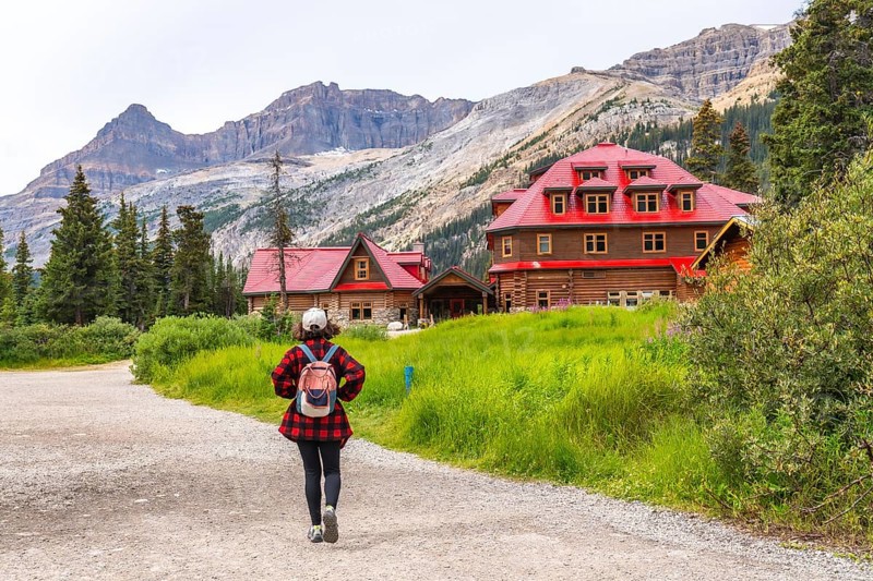 Female tourist walking on a gravel path towards the historic num ti jah lodge at bow lake in the canadian rockies of banff national park, alberta, with stunning mountain scenery in the background
