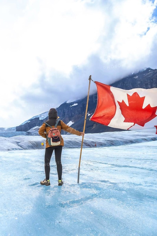 Tourist is holding large canadian flag while standing on athabasca glacier in jasper national park, a popular tourist destination in the canadian rockies known for its stunning natural beauty