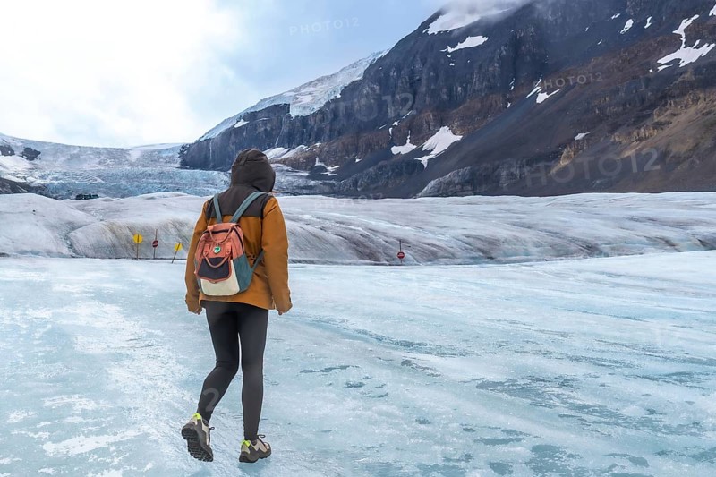 Tourist walking on the surface of athabasca glacier in jasper national park in the canadian rockies of alberta, canada, enjoying the stunning views of the mountains and ice formations