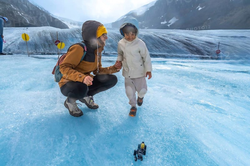 Mother and child enjoying playful moments on the athabasca glacier, with a toy vehicle in the foreground and the majestic canadian rockies in the background
