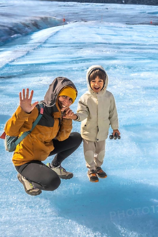 Mother and her son are enjoying their visit to the athabasca glacier in jasper national park, alberta, canada, waving and smiling amidst the stunning blue ice