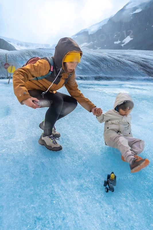 Tourist mother helping her child after slipping on the ice surface of the athabasca glacier in jasper national park, showcasing the beauty and potential hazards of glacial environments