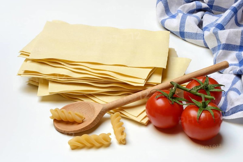 Lasagna, dried lasagna leaves and fusilli noodles with tomatoes and cooking spoon