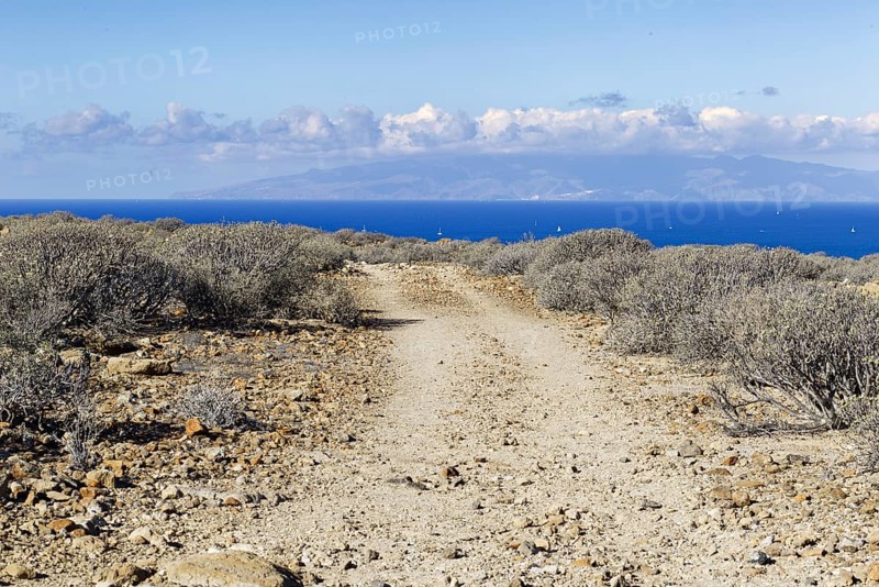A hiking trail leads through the barren landscape with views of the distant sea, Los Cristianos Tenerife