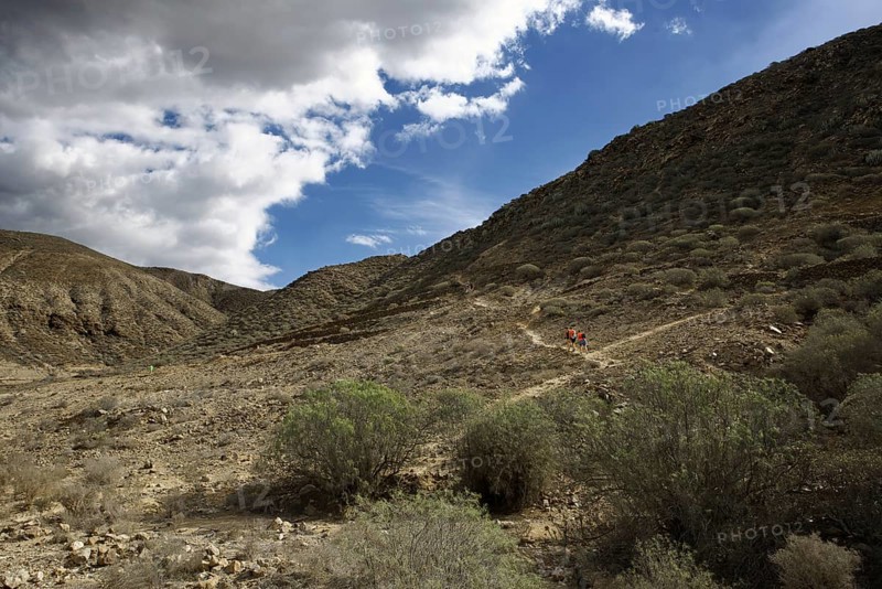 Barren mountain landscape with hikers in the distance and cloudy sky, Los Cristianos Tenerife