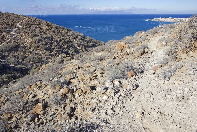 A dry trail snakes through a rocky coastal landscape with views of the sea, Los Cristianos Tenerife