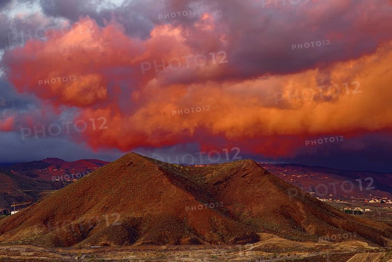 Dramatic cloud formations in shades of red over a mountainous landscape at sunset, Los Cristianos Tenerife