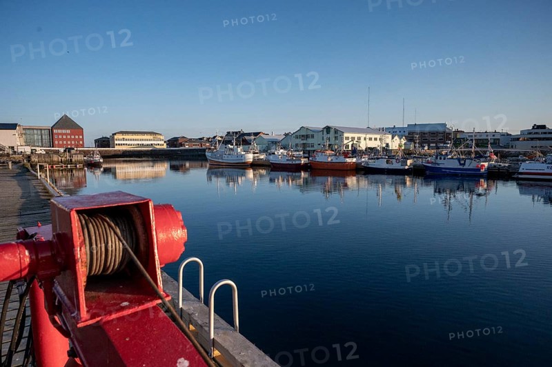 Idyllic harbor with calm water, several boats and buildings in the background under clear skies, Vardø, Finnmark, Norway