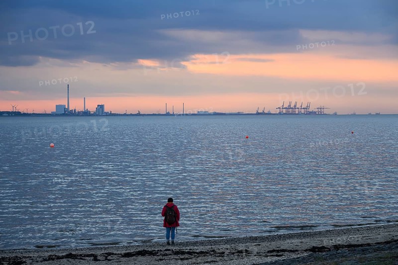 Person on the beach with a view of the sea and industrial areas in Wilhelmshafen right Jade-Weser Port, blue-orange twilight, Eckwarderhörne, Butjadingen, Lower Saxony, Germany