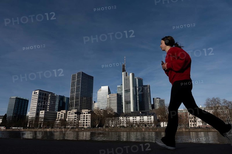 A female jogger walks past the banks of the Main in front of Frankfurt's banking skyline, Mainufer, Frankfurt am Main, Hesse, Germany